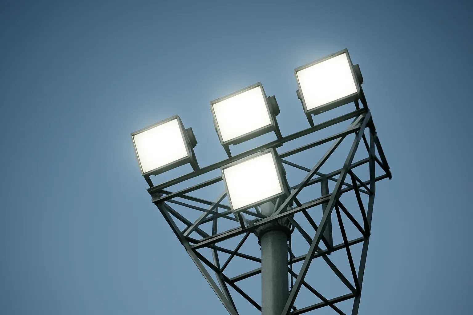 Looking up at four bright stadium lights through metal structure